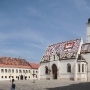 The colourful St Mark's Church, with its unique tiled roof constructed in 1880. The tiles on the left side depict the medieval coat of arms of Croatia, Dalmatia and Slavonia, while the emblem of Zagreb is on the right side. The 13th-century church was named for the annual St Mark's fair, which was held in Gradec at the time, and it retains a 13th-century Romanesque window on the southern side.<br />The Gothic portal composed of 15 figures in shallow niches was sculpted in the 14th century. The present bell tower replaces an earlier one that was destroyed by an earthquake in 1502. The interior contains sculptures by Meštrović.