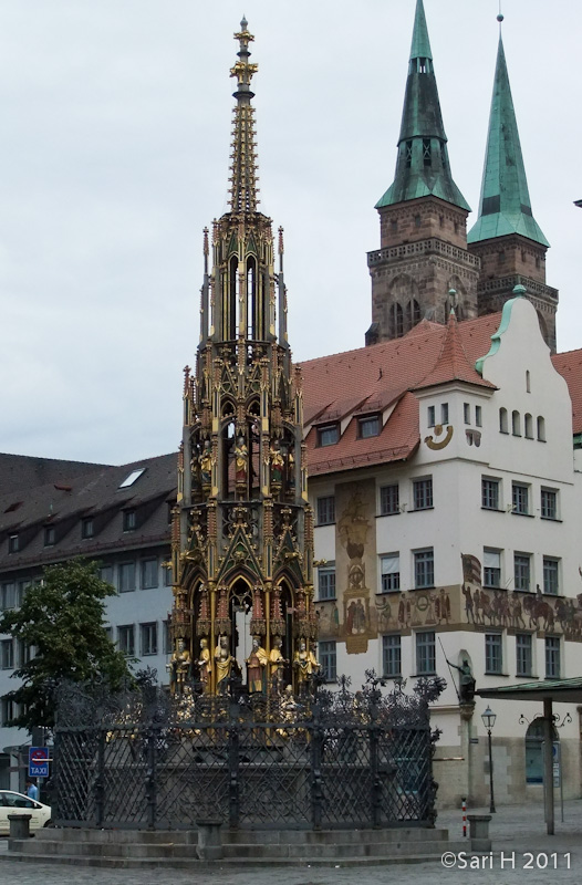 nurmberg-26.jpg - Schöner Brunnen (Beautiful Fountain). Erected between 1389 and 1396 by the builder and stonemason, Heinrich Beheim, the 19-metre stone pyramid rises from the octagonal basin like a Gothic steeple top, narrowing in three steps, right to the top finial. Forty stone figures are arranged in three rows, all of them important 14th century sculptures representing the world-view of the Holy Roman Empire: in the bottom row allegorical figures symbolising Philosophy and the Free Arts, in the middle row the evangelists and Latin Church Fathers, in the third row the seven electors and nine heroes, at the very top Moses and the seven prophets.